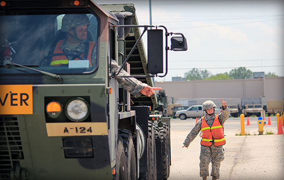 Indiana Army National Guard Pfc. William Weikel (left) operates a M1120 Heavy Expanded Mobility Tactical Truck (HEMTT) Load Handling System truck while Ohio Army National Guard Spc. Kaitlin Torgerson directs him using proper hand-and-arm signals .