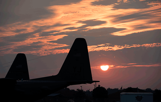 The sun rises over a C-130H Hercules on the flight line.