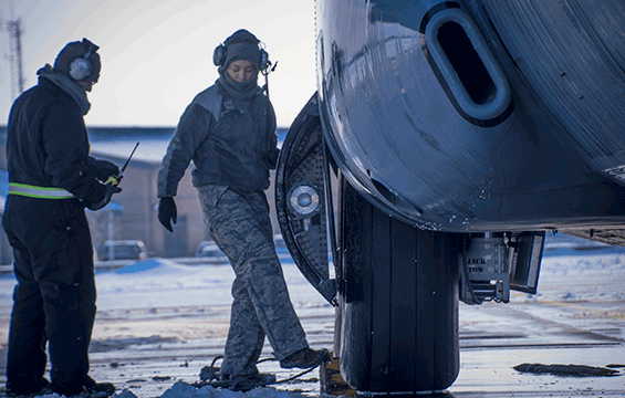 Airmen adjust a wheel chock under the tire of a C-130H Hercules during bitter cold temperatures.
