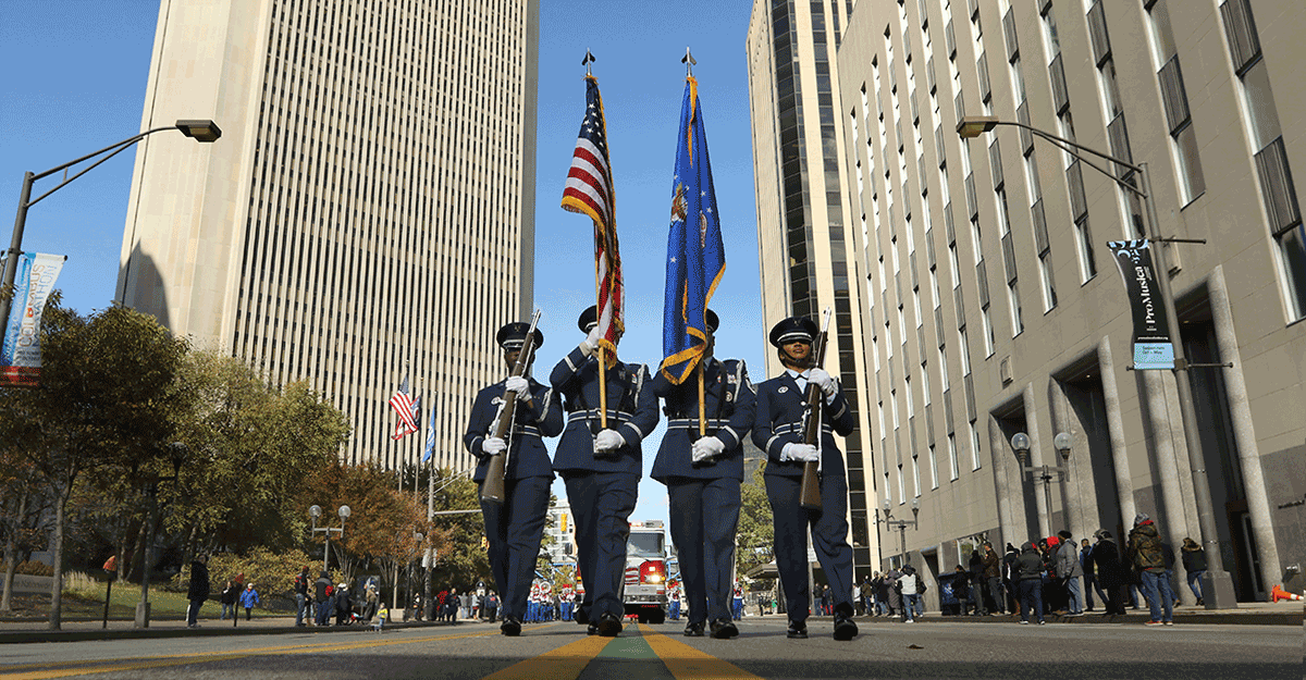 Color Guard carry flags in middle of street in downtown Columbus during parade.
