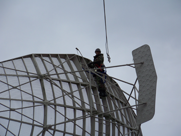 An Airman with the 212th Engineering Installation Squadron, out of Milford, Mass., waits for the rigging so he can attach it to the lifting points on the L-band antenna in preparation for its removal. 