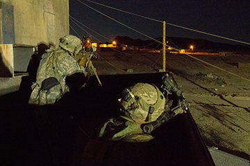 Soldiers scan a deserted street for enemy combatants during a nighttime assault.