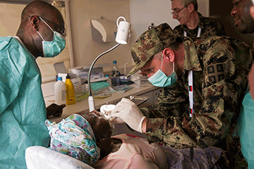 Soldier performing dental procedure on local woman.