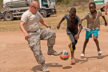 Guard member playing soccer with a couple local boys 
