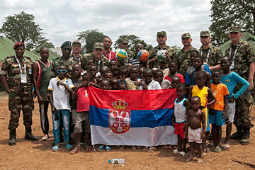 Serbian members pose with local children holding a Serbian flag