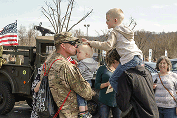 Soldier holds toddler, greets family.
