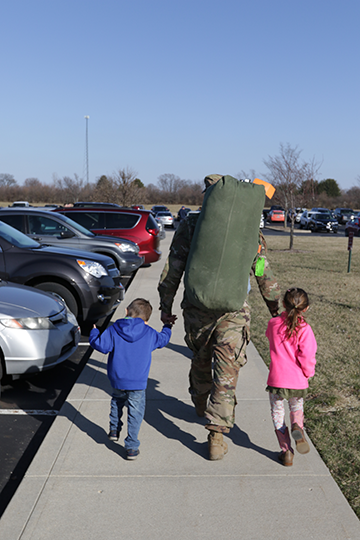 Soldier leaves hand in hand with children.