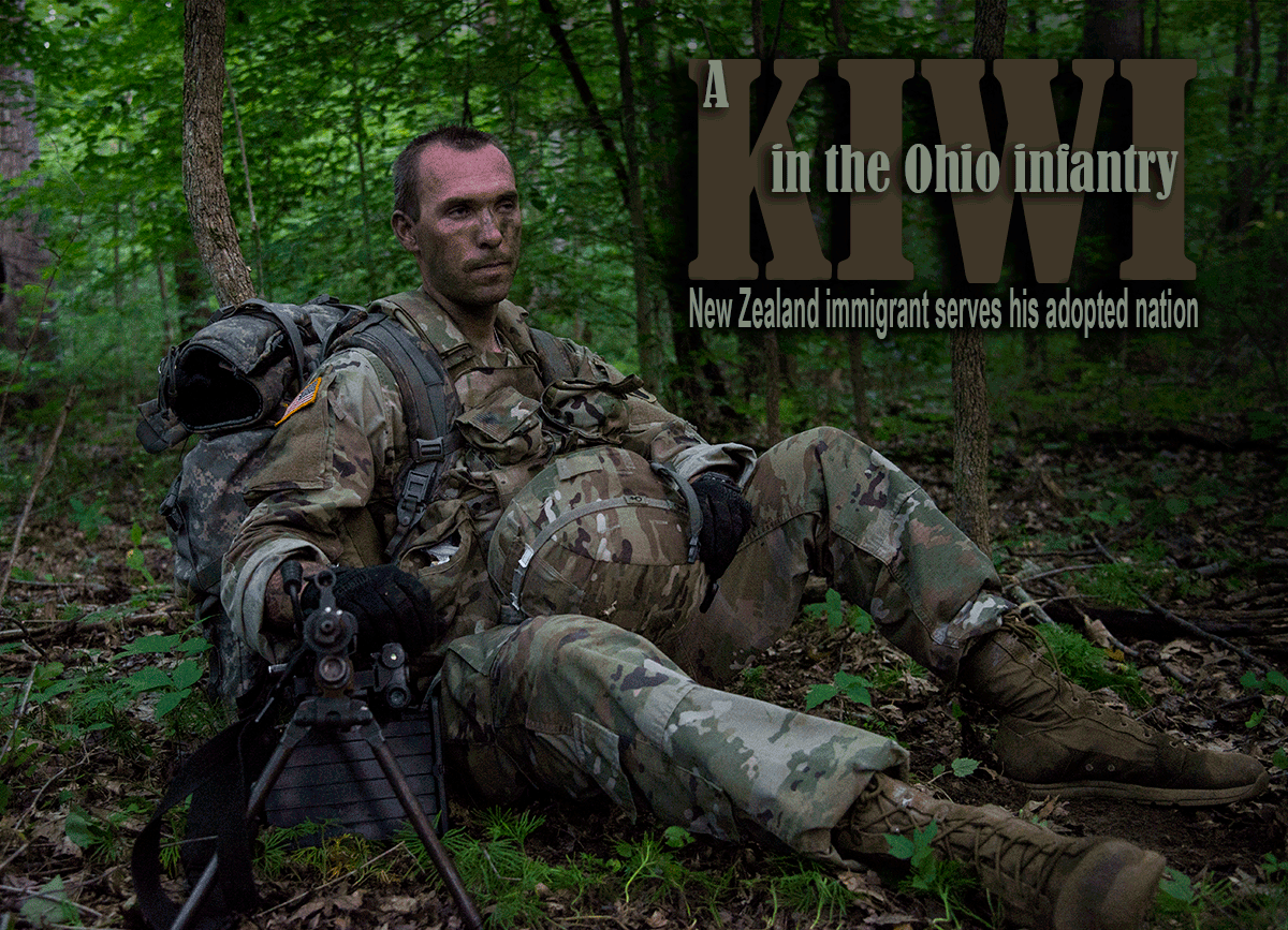 Soldier in camo sits in forest.