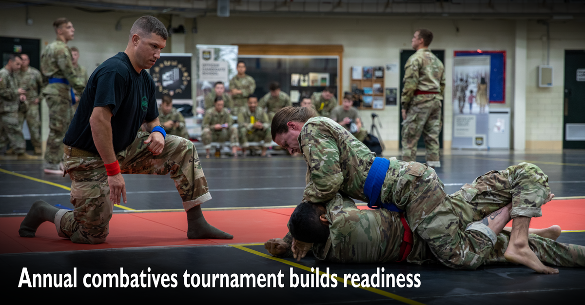 Female soldiers wrestle on mat during competition.