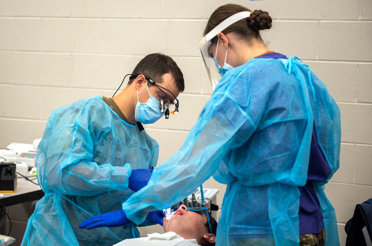 Airmen in blue scrubs work on patient's mouth