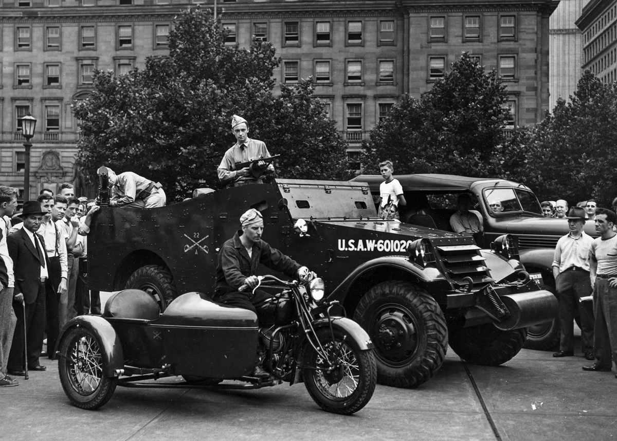 Soldiers in front of jeep and motorcycle sidecar in city.