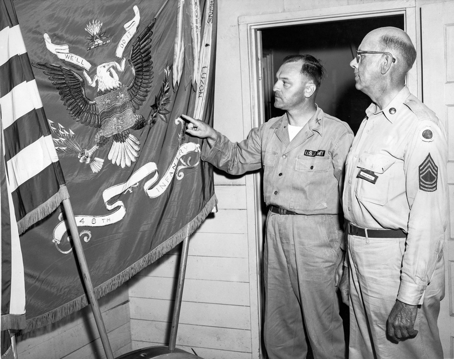 Black and white photo of commanders pointing at 148th flag.