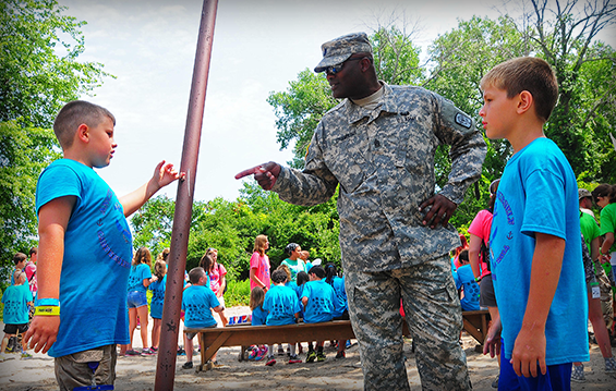 Command Sgt. Maj. Sheldon Chambliss, command sergeant major of the 2nd Battalion, 174th Air Defense Artillery Regiment, speaks with two youth campers.