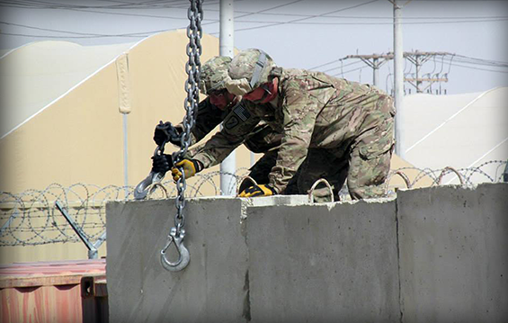 Two Soldiers assigned to the 1191st Engineer Company attempt to hook a jersey barrier to a crane.