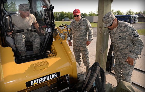 Staff Sgt. Christopher Larson (in red cap), North Dakota Air National Guard Regional Training Site instructor, oversees the operation of a skid steer loader by Senior Airman Joel Coppola (left), of the Ohio Air National Guard’s 121st Air Refueling Wing, as Master Sgt. Philip Murray, also of the 121st Air Refueling Wing, assists.