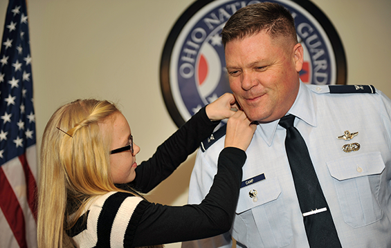 Col. James Camp, director of human resources for the Ohio National Guard, receives his eagle O-6 rank shoulder epaulette from his daughter, Remy.