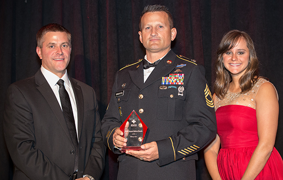 Tim Petska (left) and Brittany Seider (right), of the American Red Cross Associate Board, present an award to Master Sgt. Matthew Sheaffer.