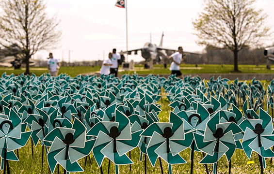 Field of teal pinwheels with runners and aircraft in background.