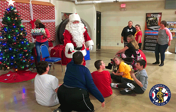 Santa with kids sitting on floor around awaiting their gifts.