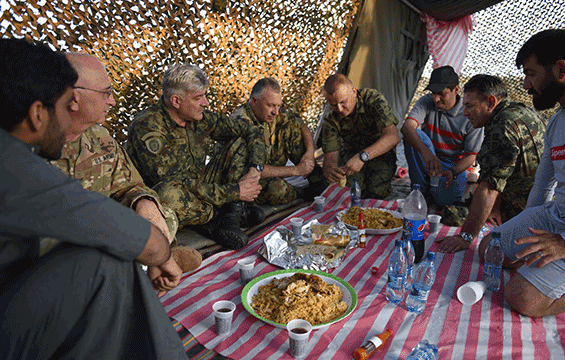 Soldiers sitting on floor of tent, sharing local prepared meal.
