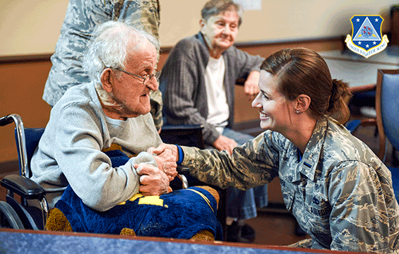 Airman kneels to shake hands with old man in wheelchair at the nursing home.