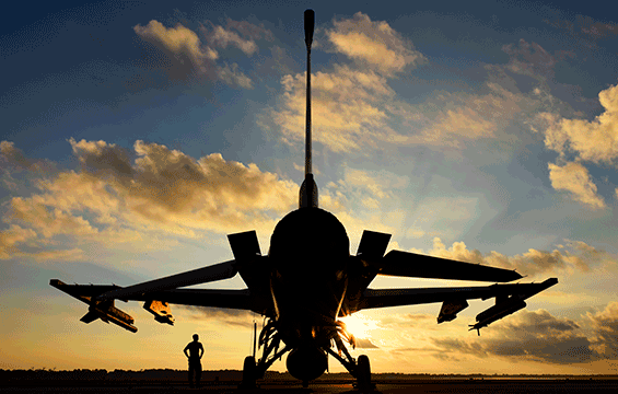Silhouette of airman on ground level under aircraft at sunset.
