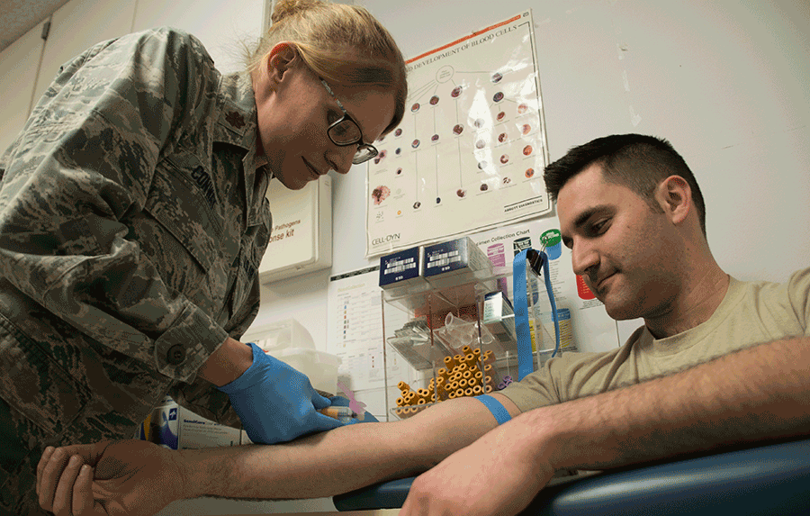 Airman prepares to draw blood from another airman.