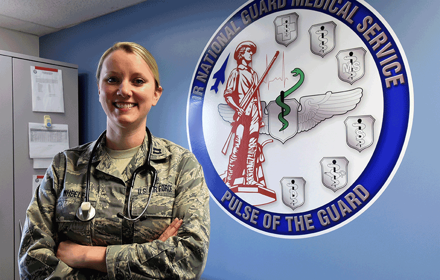 Capt. Rachael Wheeler poses in front of logo on wall.