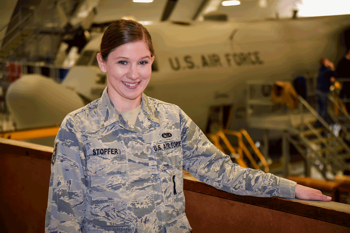 Staff Sergeant Heather Stoffer poses at in hangar with U.S.AIR FORCE aircraft in background.