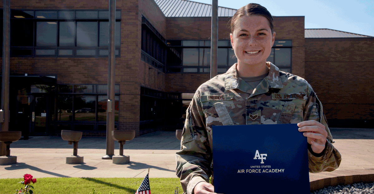 Female Airman poses with Academy certificate in fron t of building.