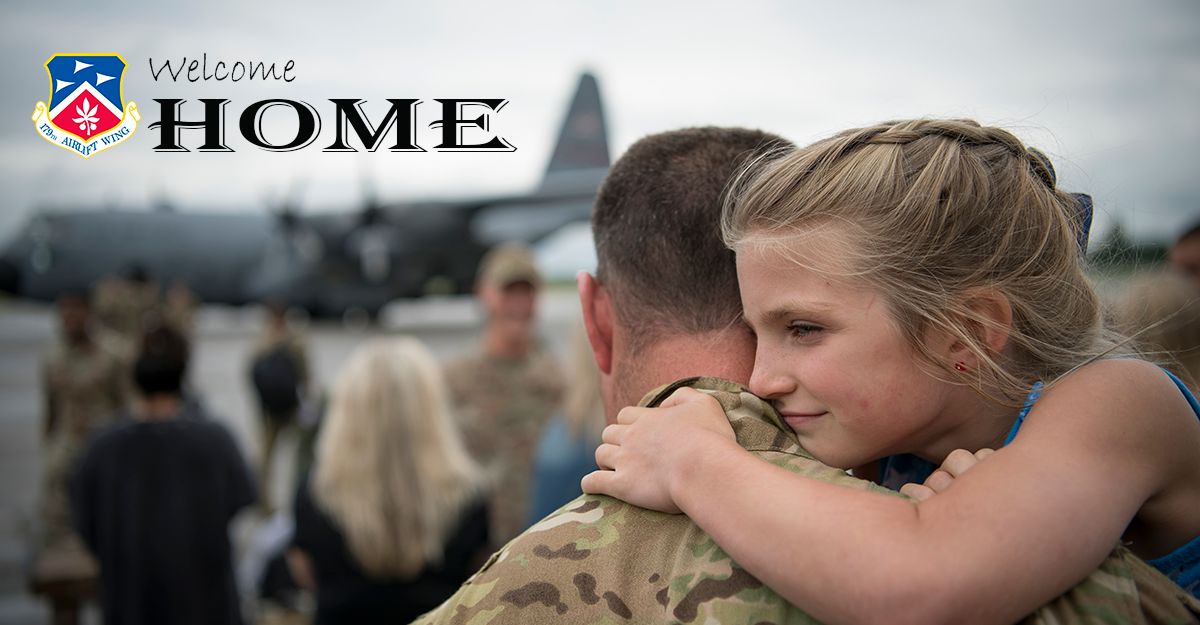 Airman holds daughter with crowd in background.
