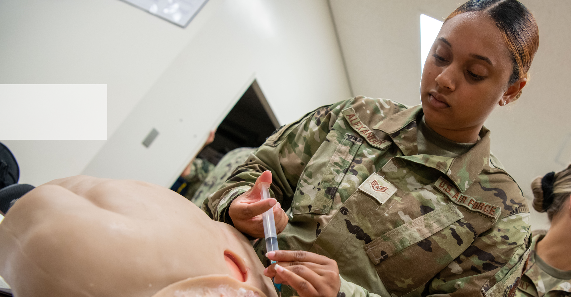 An aerospace medical technician performs a procedure on a training mannequin