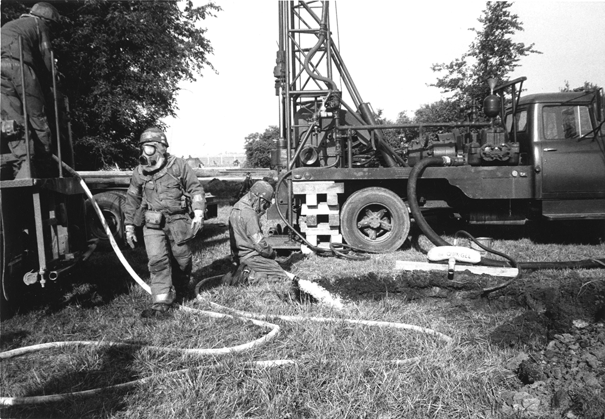 Members of the 200th RED HORSE operate a water well driller in chemical suits.