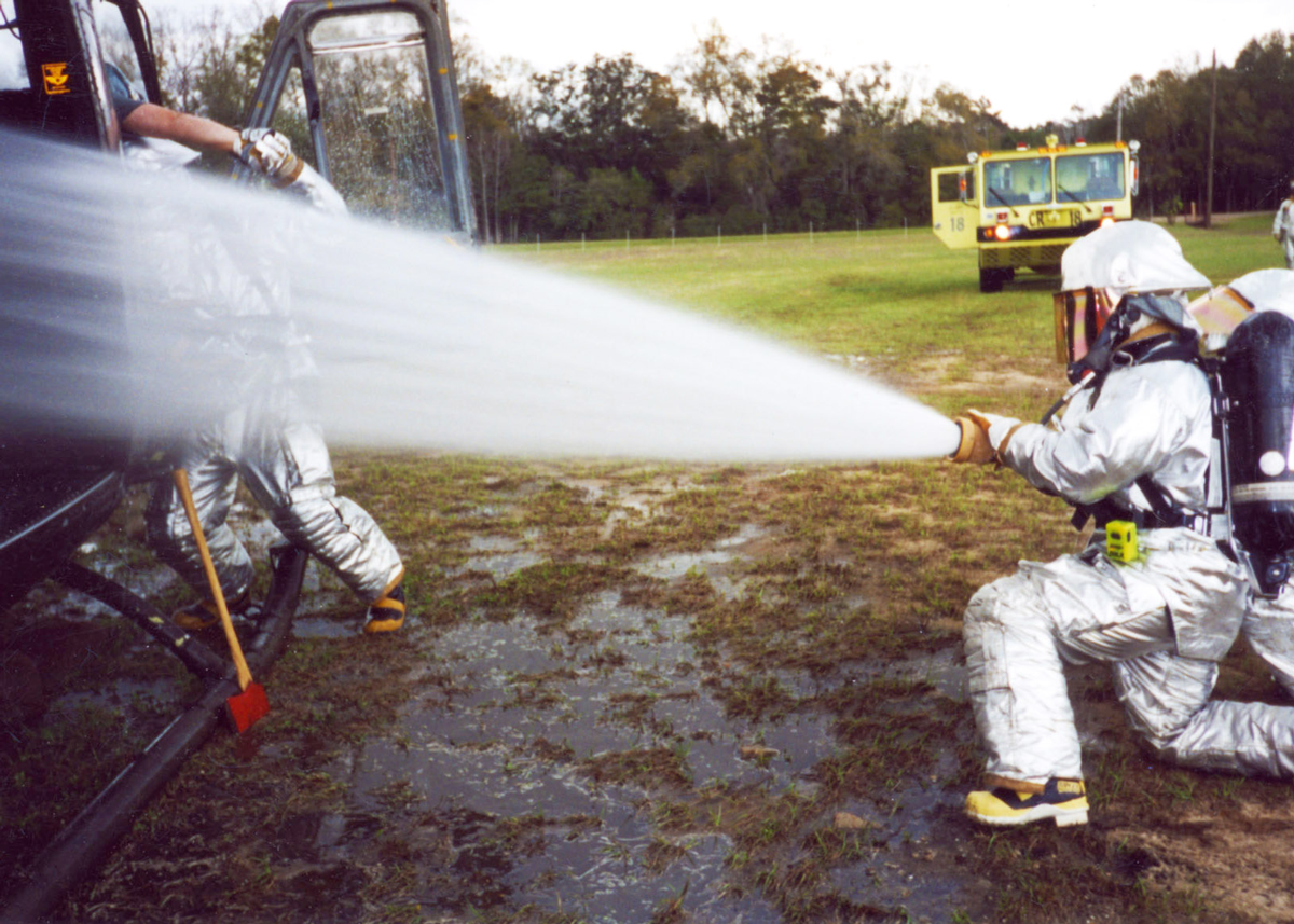 Color photo of Soldier in hazmat suit spraying fire hose.
