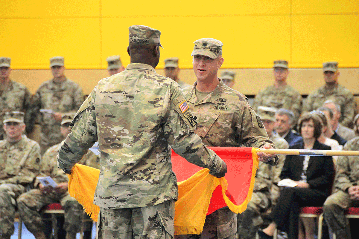 Commanders hold flag while Soldiers sit in audience to watch.