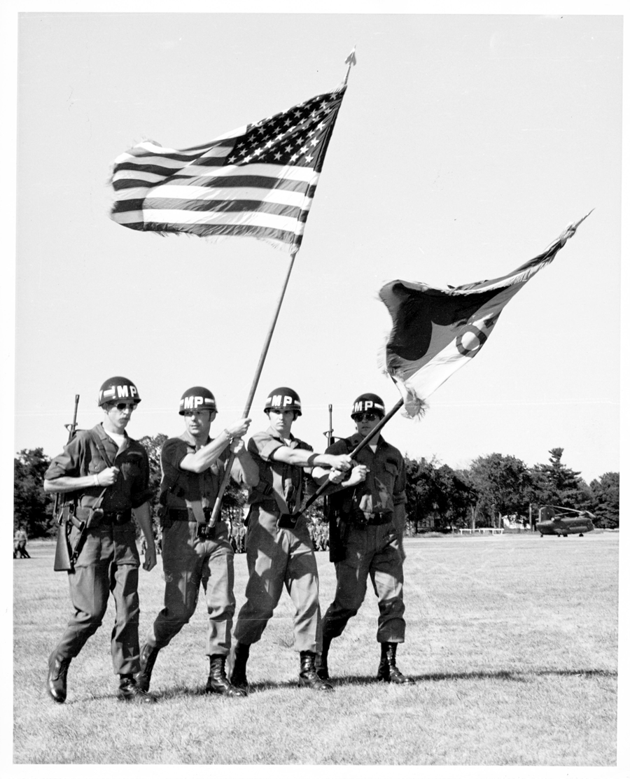 Black and white image of color guard carrying flags.