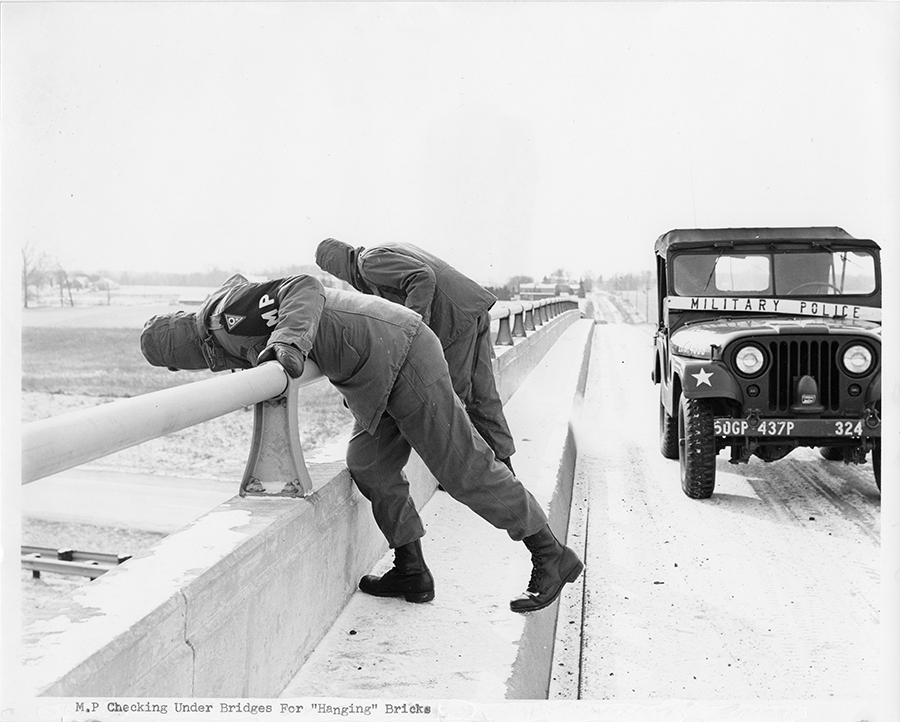 Black and white photo of Soldiers looking over railing on overpass from 1970..