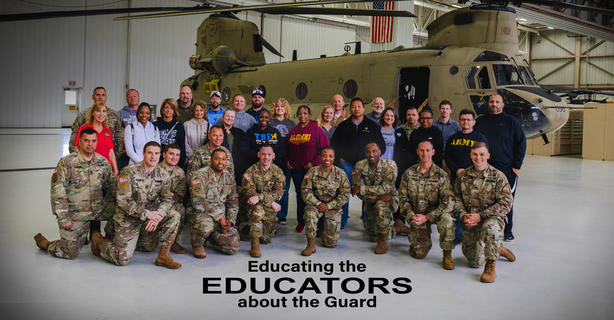 Guard members pose with educators in front of helicopter.