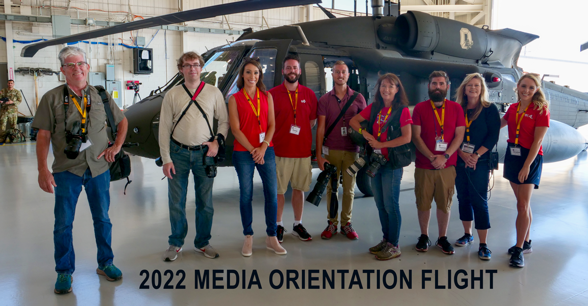 Group of media personnel and photographers pose in front of a BlackHawk.