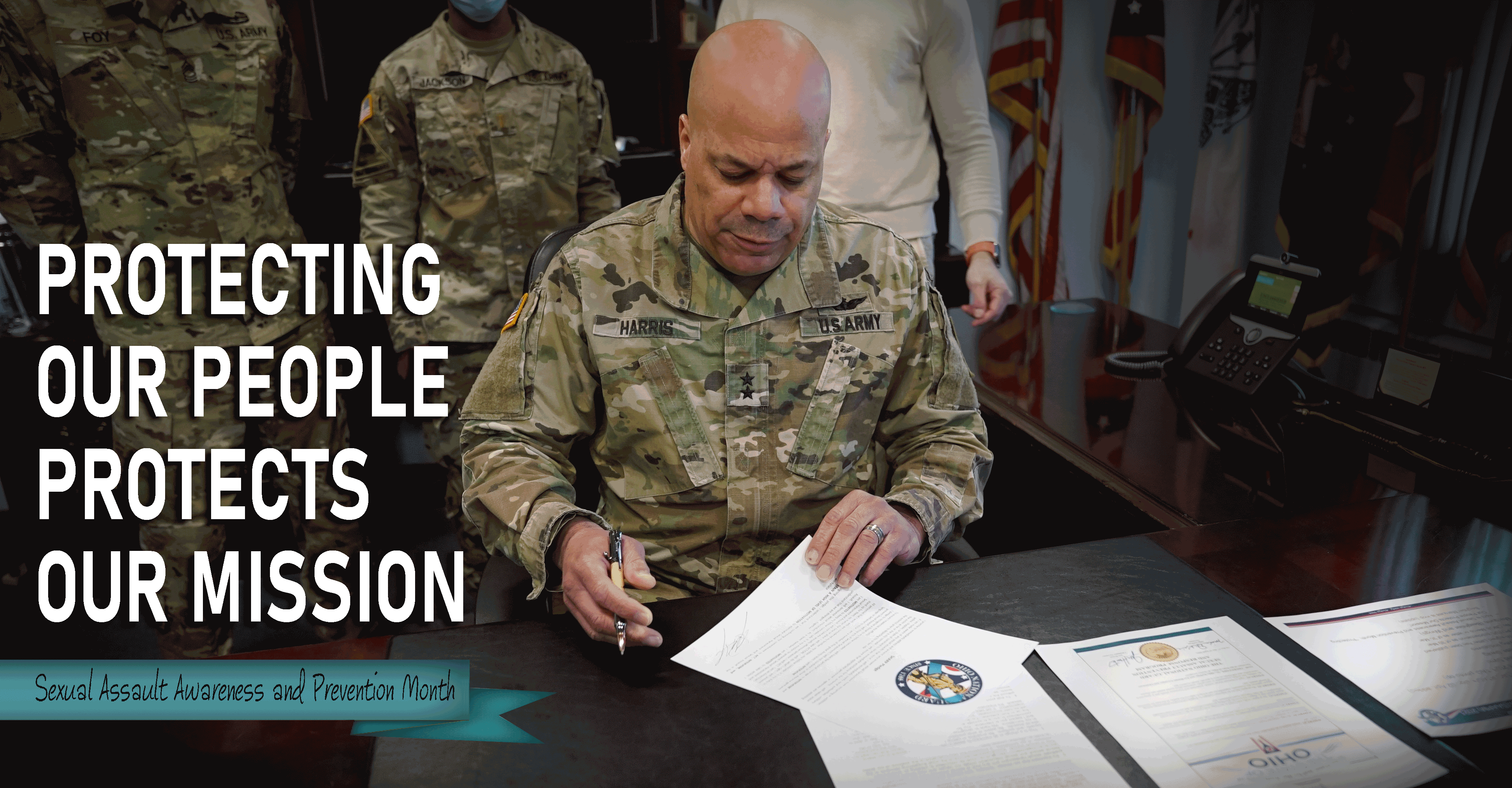 Ohio Adjutant General signs documents on  his desk as Guard Members stand behind.
