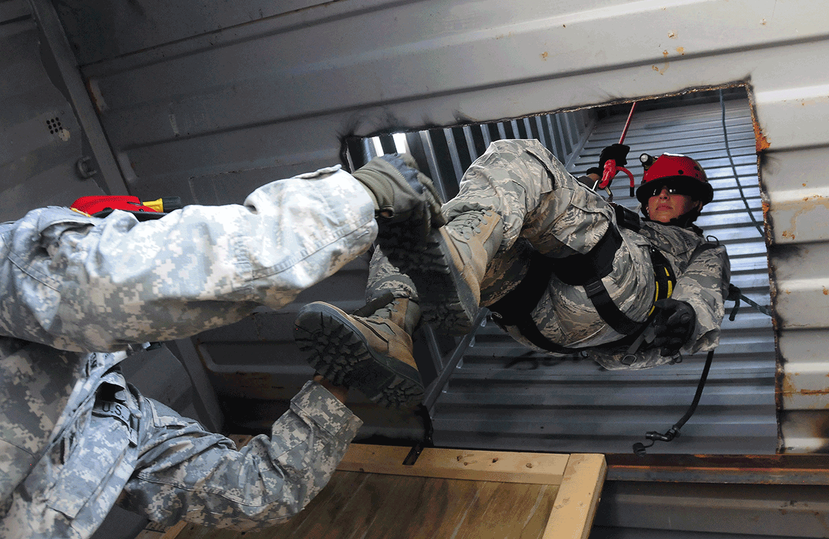 Guard member assists fellow airman descending from rope.