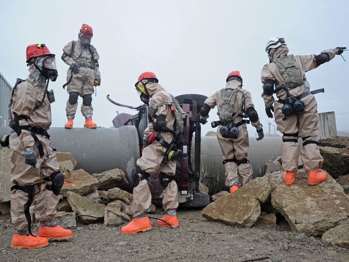 Airmen in hazmat suits gather around rubble and concrete pipe.
