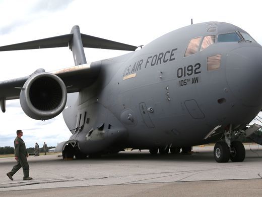 A member of the Ohio National Guard walks past a C-17 being loaded with heavy equipment.