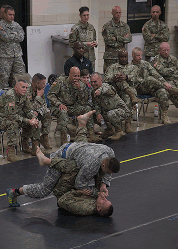 Two soldiers compete on mats while ONG members watch.