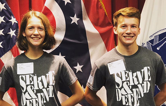 Teenage brother and sister stand in fornt of Ohio flag wearing t-shirts that read: Serve & Defend