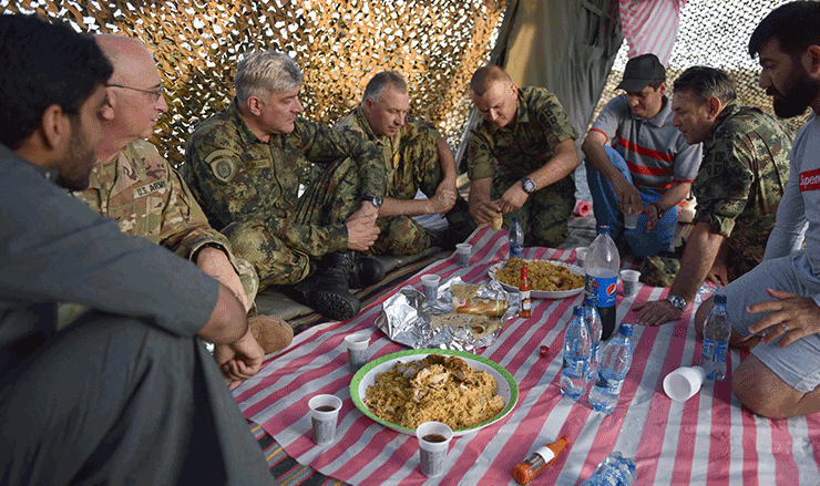 Representatives from Serbia and Ohio sit on ground in tent to share a traditional Halal meal.