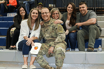 Soldier poses with his family on bleachers.