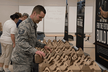 Airman looks over box lunches on table display.