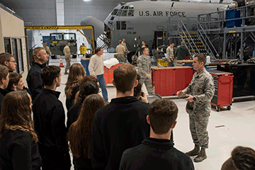 Alexander talks to recruits in hangar in fornt of aircraft.