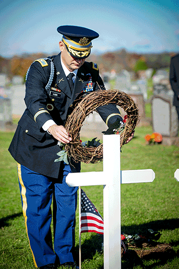 Soldier places wreath on cross monument.